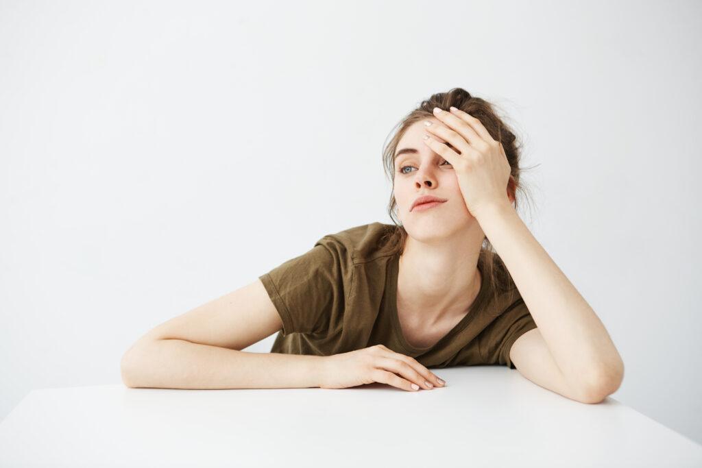 bored tired dull young woman student with bun sitting table white background